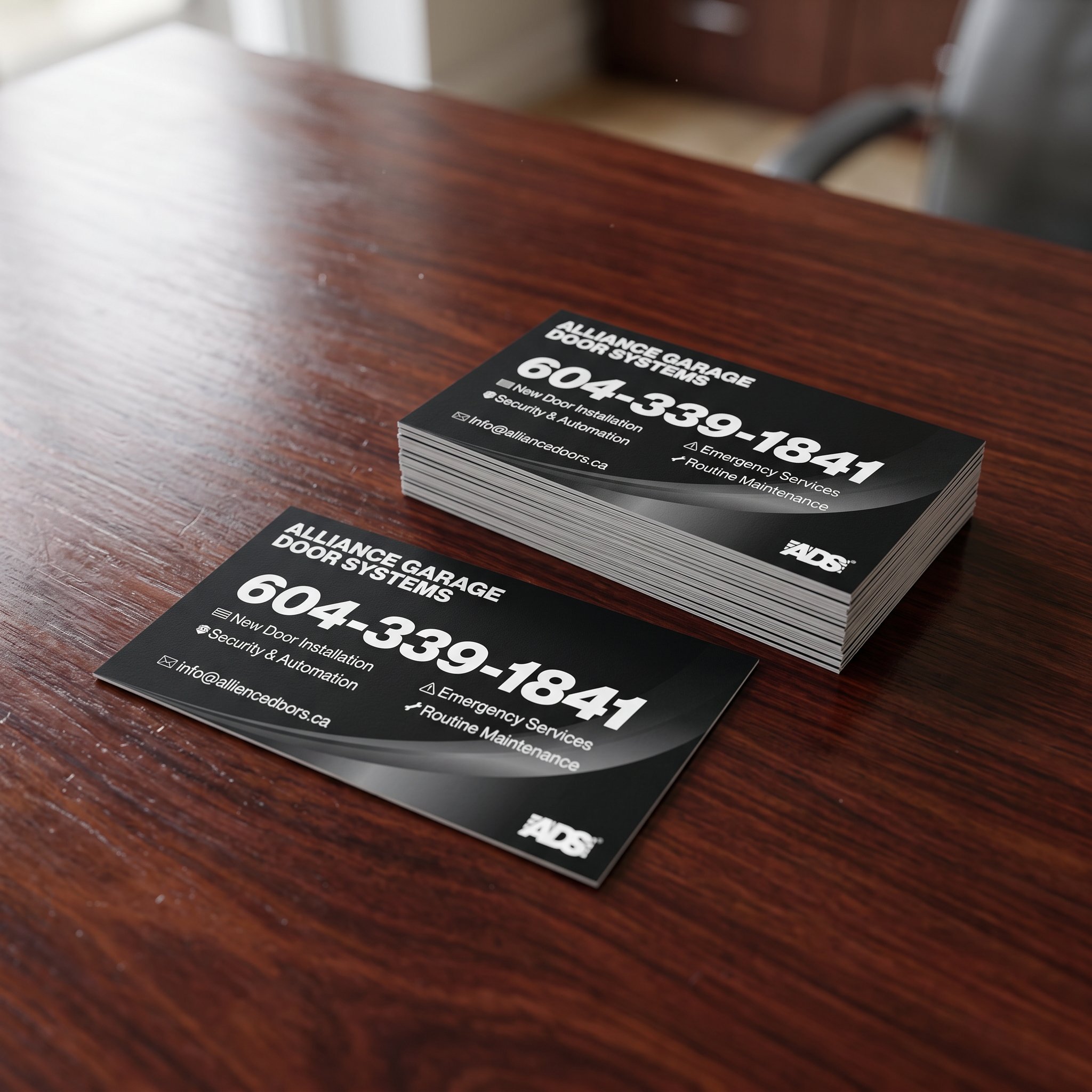 Stack of black ADS business cards on a wooden desk, with the phone number set large in white