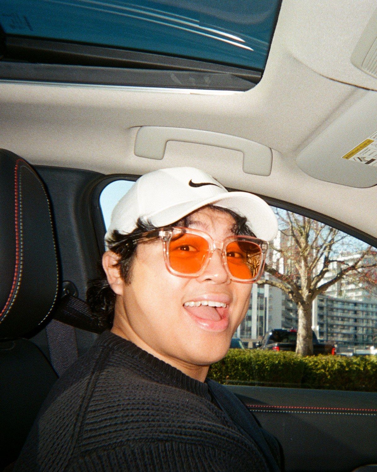 Portrait of Matthew Subade in a car, wearing a white Nike cap and orange-tinted sunglasses
